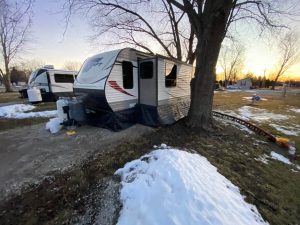 Insulated RV skirting is installed on a bumper pull camper with snow on the ground nearby.