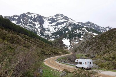 A motorhome is driving along a dirt road in the mountains.