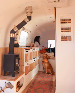 A DIY Tiny Wood Stove is featured in a bright and cozy bumper pull RV.